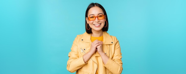 Portrait de femme asiatique à lunettes de soleil à la recherche d'espoir flatté souriant heureux debout sur fond bleu