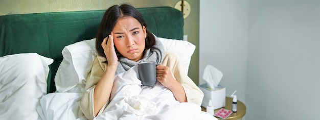 Photo gratuite portrait d'une femme asiatique souffrant de maux de tête attrapant un col qui reste en congé de maladie à la maison, allongée dans son lit