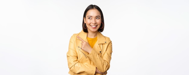 Portrait d'une femme asiatique souriante pointant et regardant à gauche en choisissant un élément montrant un logo ou un support de bannière