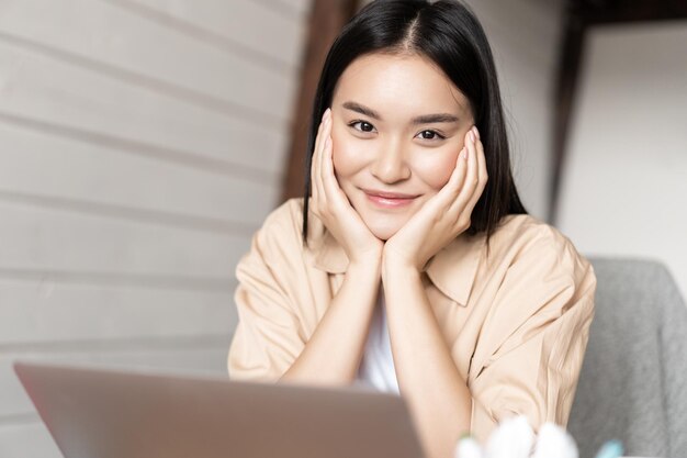 Portrait d'une femme asiatique souriante travaillant sur un ordinateur portable depuis la maison se reposant avec un ordinateur assis détendu dans...