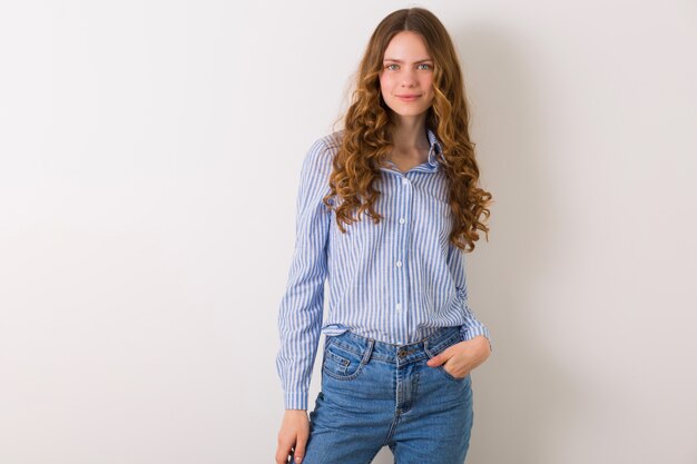 Portrait de femme assez naturelle ypung posant en chemise en coton rayé bleu contre blanc