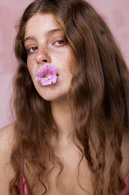 Portrait de femme aux taches de rousseur avec fleur dans sa bouche