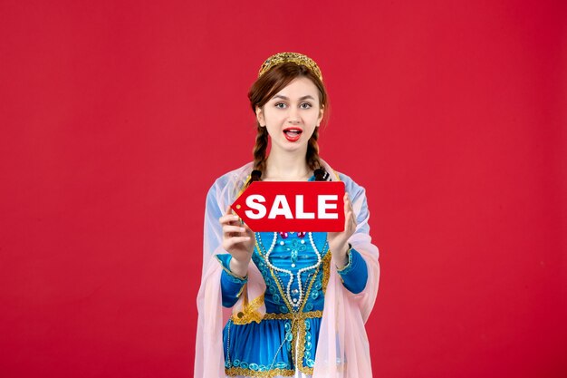 Portrait de femme azérie en costume traditionnel tenant la plaque signalétique de la vente sur le rouge