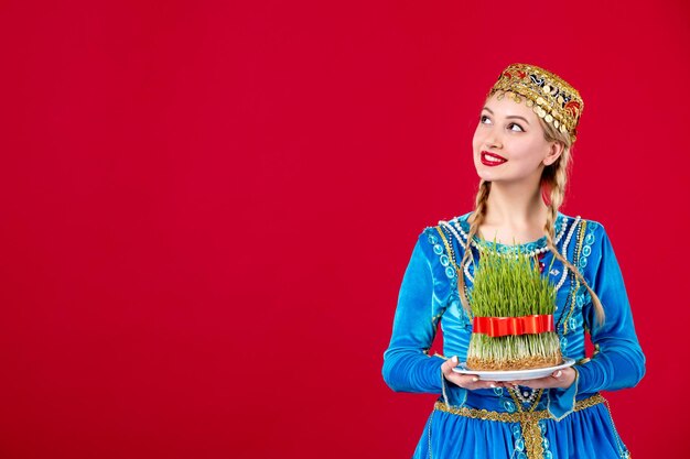 Portrait de femme azérie en costume traditionnel tenant semeni tourné en studio sur fond rouge photo ethnique printemps concept novruz