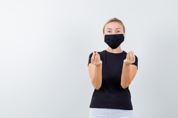 Portrait de femme blonde faisant un geste italien en t-shirt noir isolé