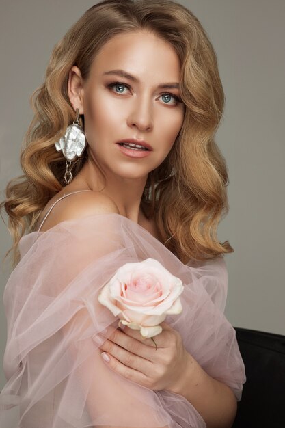 Portrait de femme blonde de luxe avec un maquillage parfait posant tenant une rose rose