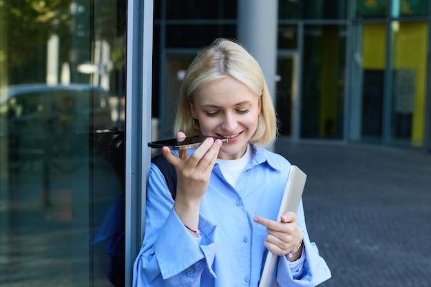 Portrait d'une femme blonde souriante écoutant un message enregistré sur un smartphone et ayant l'air heureuse