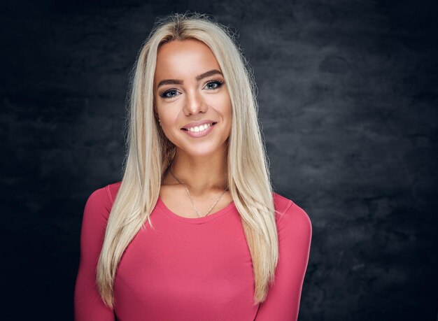 Portrait d'une femme blonde souriante vêtue d'un maillot de sport rose sur fond gris.