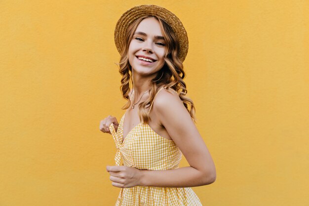 Portrait de femme bouclée à la mode souriant. Tir intérieur d'un modèle féminin mignon en robe rétro et chapeau.