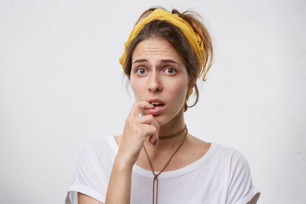 Portrait de femme bouleversée fronçant les sourcils tenant le doigt dans la bouche exprimant son doute ne sachant pas quoi choisir. Pensive jeune femme avec une apparence agréable à hésiter