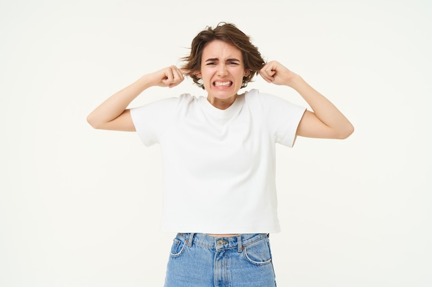 Photo gratuite portrait d'une femme bouleversée qui ferme ses oreilles en se sentant mal à l'aise à cause du bruit fort debout sur du blanc