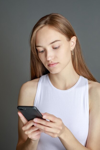 Portrait d'une femme brune de 20 ans utilisant un téléphone portable tout en se tenant isolé sur fond jaune