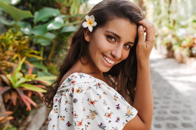 Portrait de femme brune en chemisier à imprimé floral avec fleur blanche dans ses cheveux