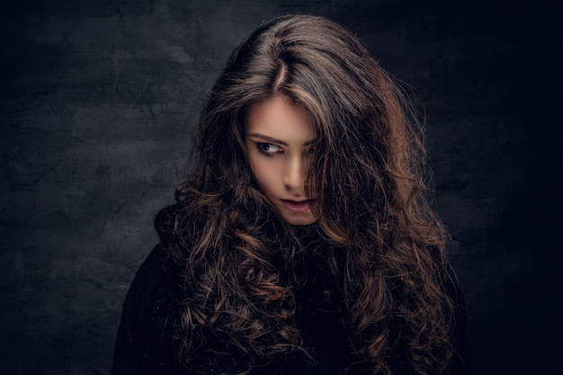 Portrait d'une femme brune sensuelle aux longs cheveux bouclés vêtue d'un pull noir chaud.