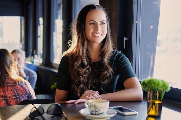 Portrait d'une femme brune souriante boit du café le matin dans un café.