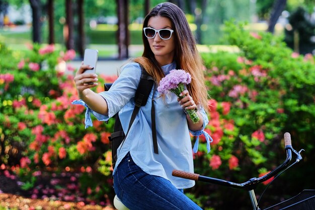 Portrait d'une femme brune sur un vélo faisant du selfie avec un téléphone intelligent.