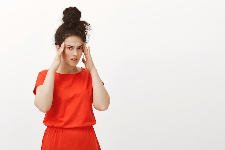 Photo gratuit portrait de femme caucasienne troublée floue en robe rouge, tenant les mains sur les tempes et fronçant les sourcils de mécontentement