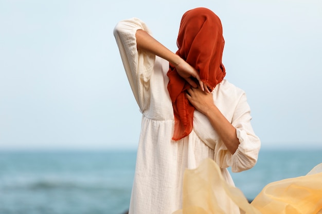 Portrait de femme couvrant son visage avec un voile à la plage