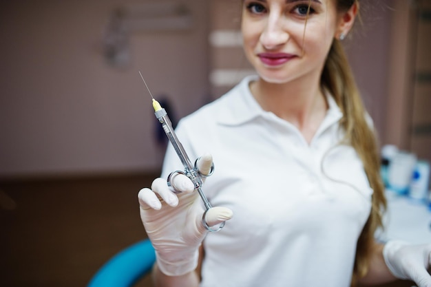 Photo gratuite portrait d'une femme dentiste en blouse blanche posant avec une seringue remplie d'anesthésie dans un cabinet dentaire