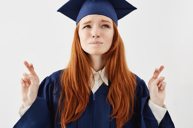 Photo gratuite portrait d'une femme diplômée rousse belle mais nerveuse en manteau priant pour le succès en tant que futur avocat ou médecin croise les doigts.