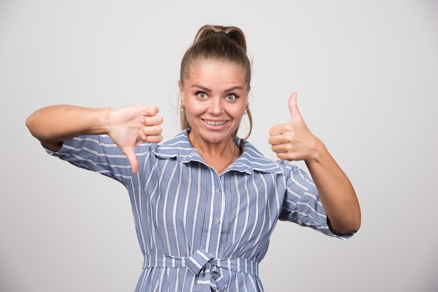 Photo gratuite portrait de femme donnant des pouces de haut en bas sur un mur gris.