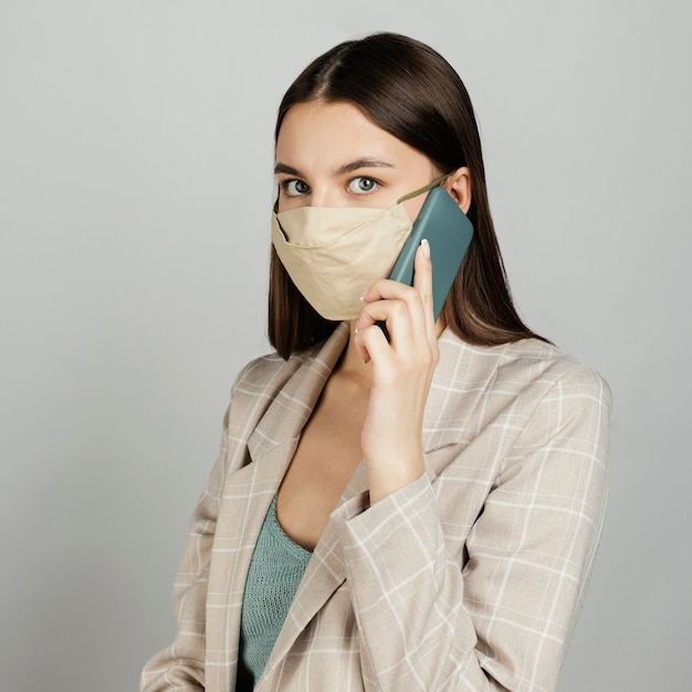 Photo gratuite portrait femme élégante avec masque à l'aide de mobile
