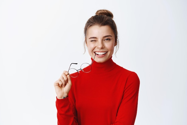 Portrait D'une Femme Entrepreneur Prospère Et Confiante, Enlevant Des Lunettes Et Une Monture De Lunettes Mordantes, Clignant De L'œil Et Souriant Sur Blanc