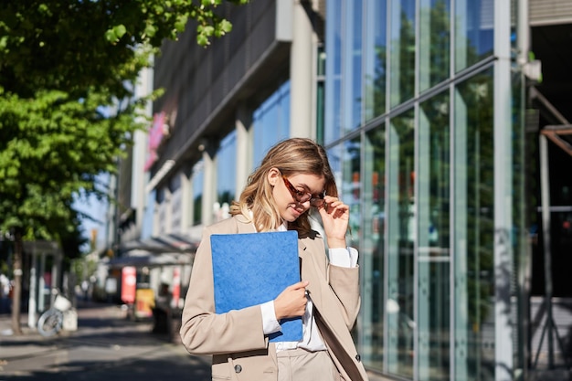 Portrait d'une femme d'entreprise confiante allant au bureau avec un dossier marchant dans la rue par une journée ensoleillée je