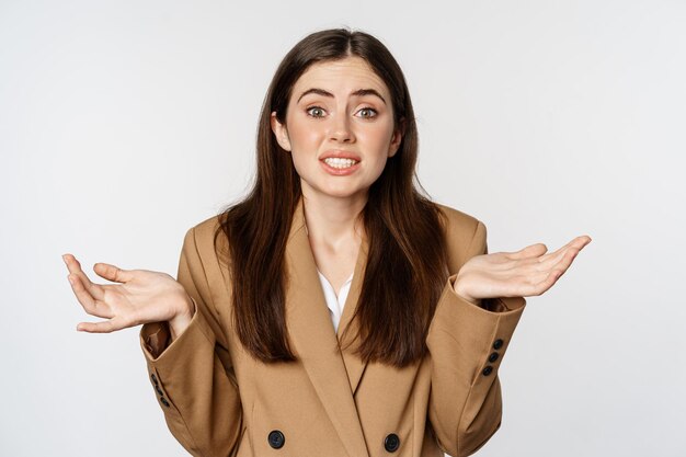 Portrait de femme d'entreprise, fille de bureau haussant les épaules et regardant désemparé, ne sais pas, perplexe, debout sur fond blanc