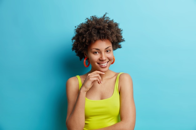 Portrait De Femme Frisée à La Recherche Agréable Garde La Main Sous Le Menton Sourit Doucement Se Sent Satisfait