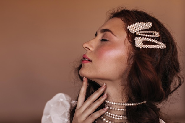 Portrait d'une femme gracieuse avec des taches de rousseur touchant doucement le cou Fille brune avec des épingles à cheveux et un collier de perles posant de profil