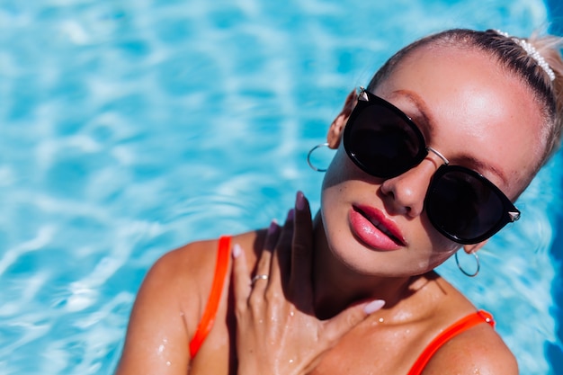 Portrait de femme heureuse calme à lunettes de soleil avec peau bronzée en bleu piscine à journée ensoleillée