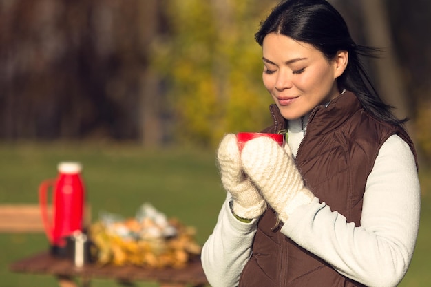 Photo gratuite portrait d'une femme heureuse passant son temps dans le parc avec une tasse rouge de thé chaud