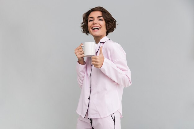 Portrait d'une femme heureuse en pyjama tenant une tasse