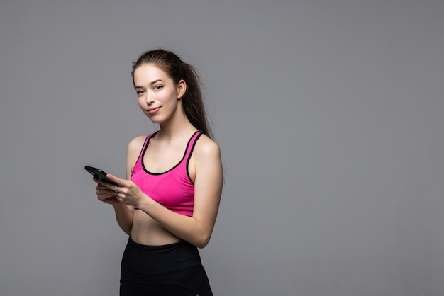 Portrait d'une femme heureuse de remise en forme debout et utilisant un téléphone portable sur blanc