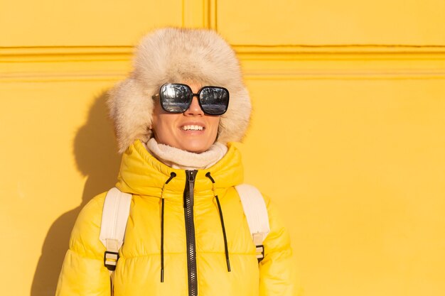 Portrait d'une femme heureuse avec un sourire en zabas blanc neige en hiver contre un mur jaune sur une journée ensoleillée dans un chapeau sibérien russe chaud