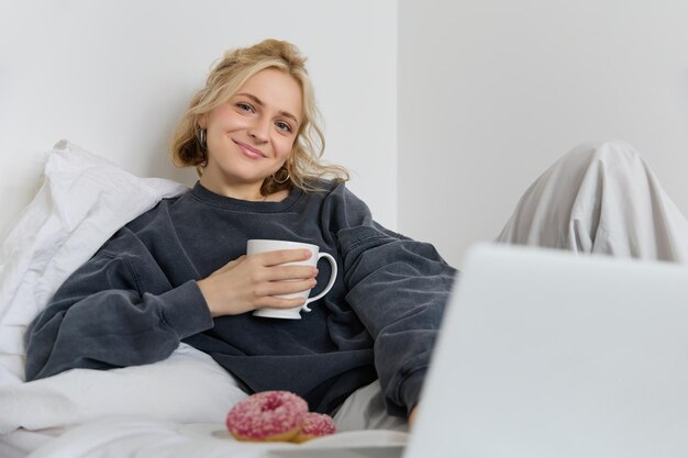 Portrait d'une femme heureuse en train de profiter d'un jour de congé à la maison allongée dans son lit en regardant une émission de télévision sur un ordinateur portable.