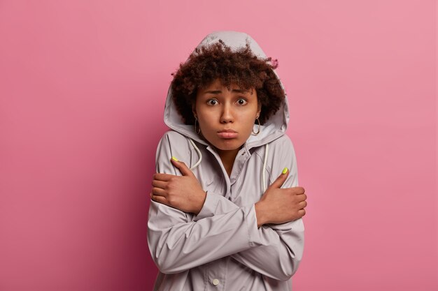 Portrait de femme insatisfaite croise les mains sur le corps, se sent gelé après avoir marché par temps humide, pose sur un mur rose, a une expression bouleversée, regarde un film d'horreur, voit une scène inattendue