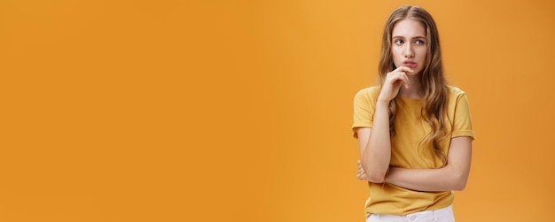 Photo gratuite portrait d'une femme intelligente concernée avec des cheveux blonds ondulés en t-shirt décontracté tenant la main sur le menton