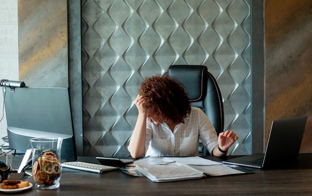 Portrait de femme jeune employé de bureau assis au bureau avec des documents et un ordinateur portable à la fatigue et surmené au bureau