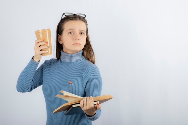 Portrait d'une femme à lunettes tenant un livre et une tasse de café.