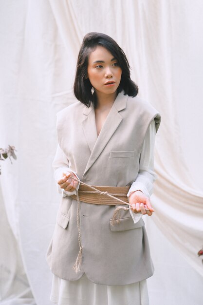 Portrait de femme magnifique au jardin, debout en robe blanche et grise pendant la journée.