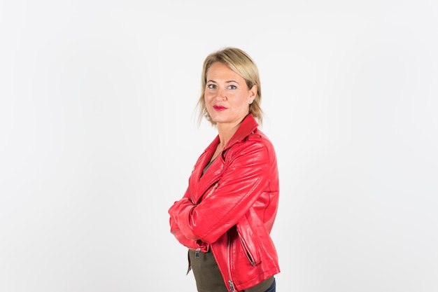 Portrait de femme mature blonde en veste de cuir rouge avec les bras croisés, debout sur un fond blanc