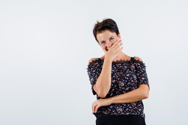 Portrait de femme mature couvrant la bouche avec la main en chemisier et à la vue de face heureux