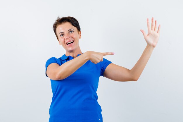 Portrait de femme mature en montrant sa main levée en t-shirt bleu et à la vue de face confiante