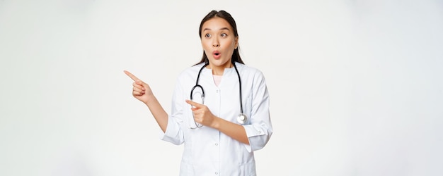 Portrait d'une femme médecin enthousiaste médecin asiatique pointant et regardant à gauche avec étonnement surpris