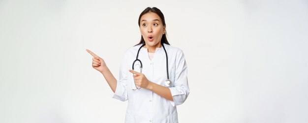 Portrait d'une femme médecin enthousiaste médecin asiatique pointant et regardant à gauche avec étonnement surpris