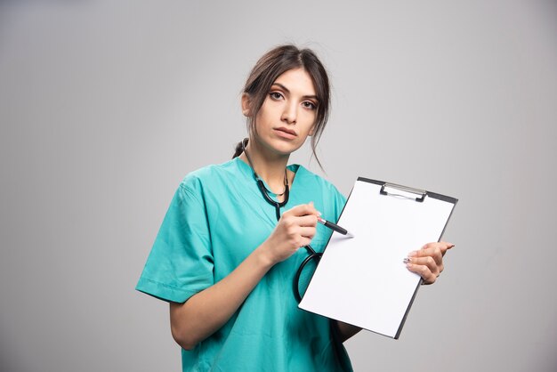 Portrait de femme médecin posant avec presse-papiers sur fond gris