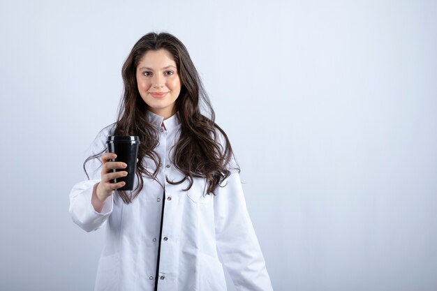 Portrait de femme médecin posant avec une tasse de café sur fond gris.