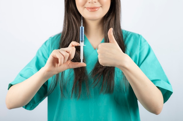 Portrait de femme médecin tenant une seringue et montrant un pouce vers le haut.